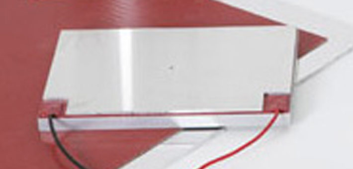 Silicone heating element attached by pressure plate with cut-out termination areas in the corners